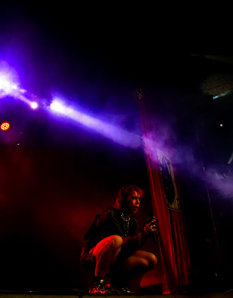 Artista agachado no palco sob feixes de luz roxa — Sad Baile Joker, Halloween em São Paulo, 17/10/2026