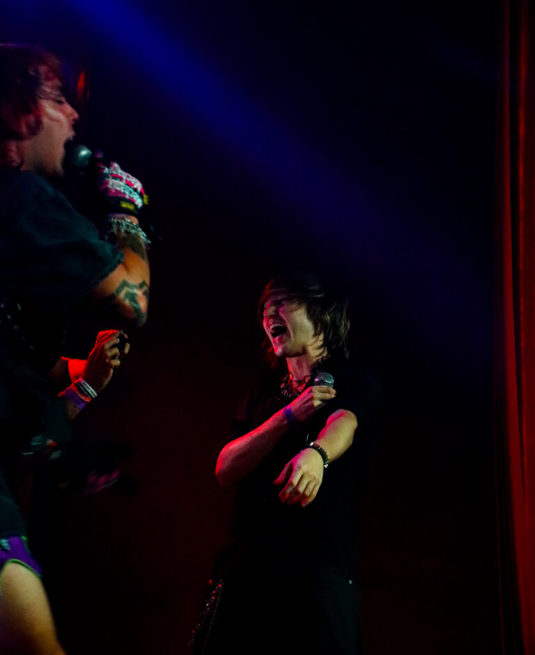 Dois artistas cantam juntos no palco sob luz azul — Sad Baile Joker, Halloween em São Paulo, 17/10/2026