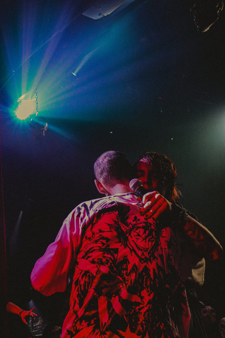 Dois artistas se abraçam no palco com holofote azul — Sad Baile Joker, Halloween em São Paulo, 17/10/2026