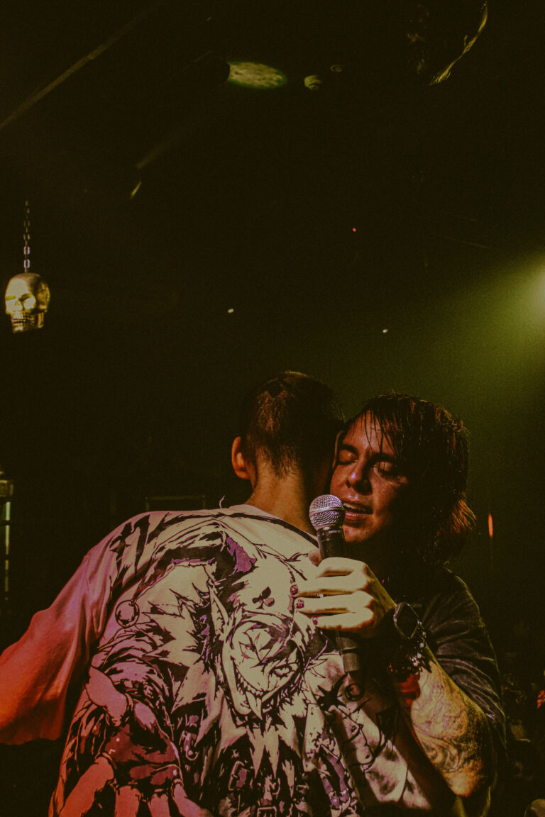 Artista canta abraçado a outro de camisa estampada — Sad Baile Joker, Halloween em São Paulo, 17/10/2026