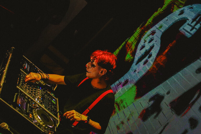DJ de cabelo vermelho mixando com o telão colorido — Sad Baile Joker, Halloween em São Paulo, 17/10/2026