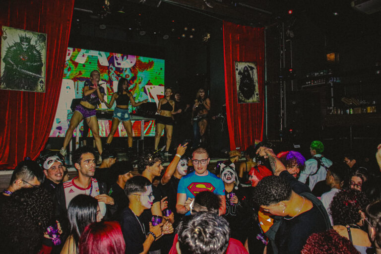Público mascarado na pista com dançarinas ao fundo — Sad Baile Joker, Halloween em São Paulo, 17/10/2026