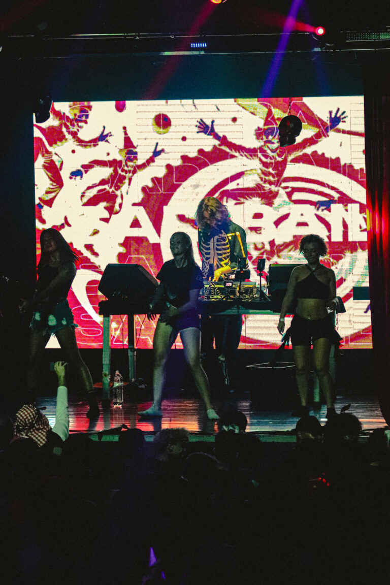 Dançarinas e DJ no palco diante do telão vermelho e branco — Sad Baile Joker, Halloween em São Paulo, 17/10/2026