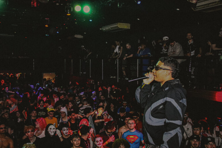 Rapper de óculos canta com o público fantasiado atrás — Sad Baile Joker, Halloween em São Paulo, 17/10/2026
