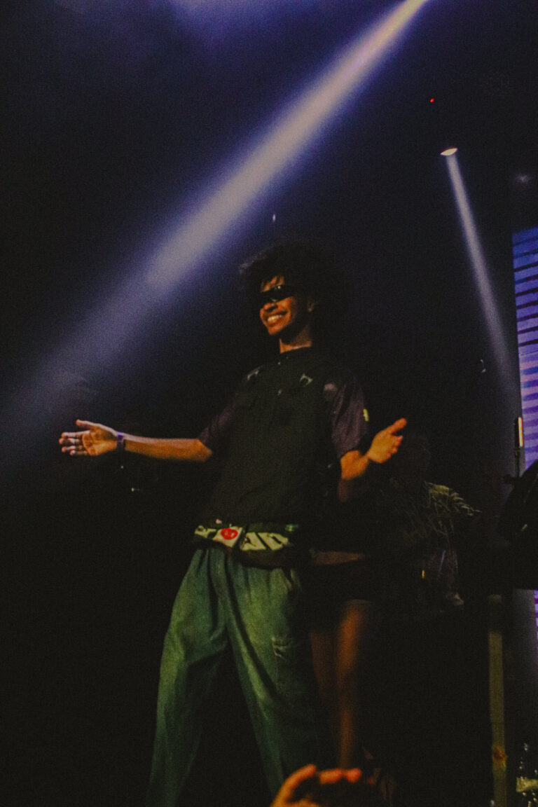 Rapper de óculos abre os braços sob feixes de luz — Sad Baile Joker, Halloween em São Paulo, 17/10/2026