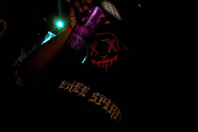 Máscara de néon vermelho com X nos olhos na pista escura — Sad Baile Joker, Halloween em São Paulo, 17/10/2026