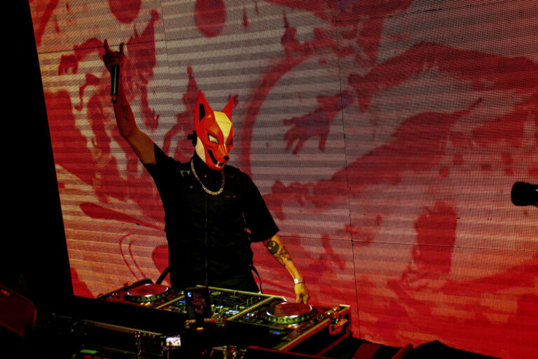 DJ de máscara vermelha diante do telão laranja — Sad Baile Joker, Halloween em São Paulo, 17/10/2026