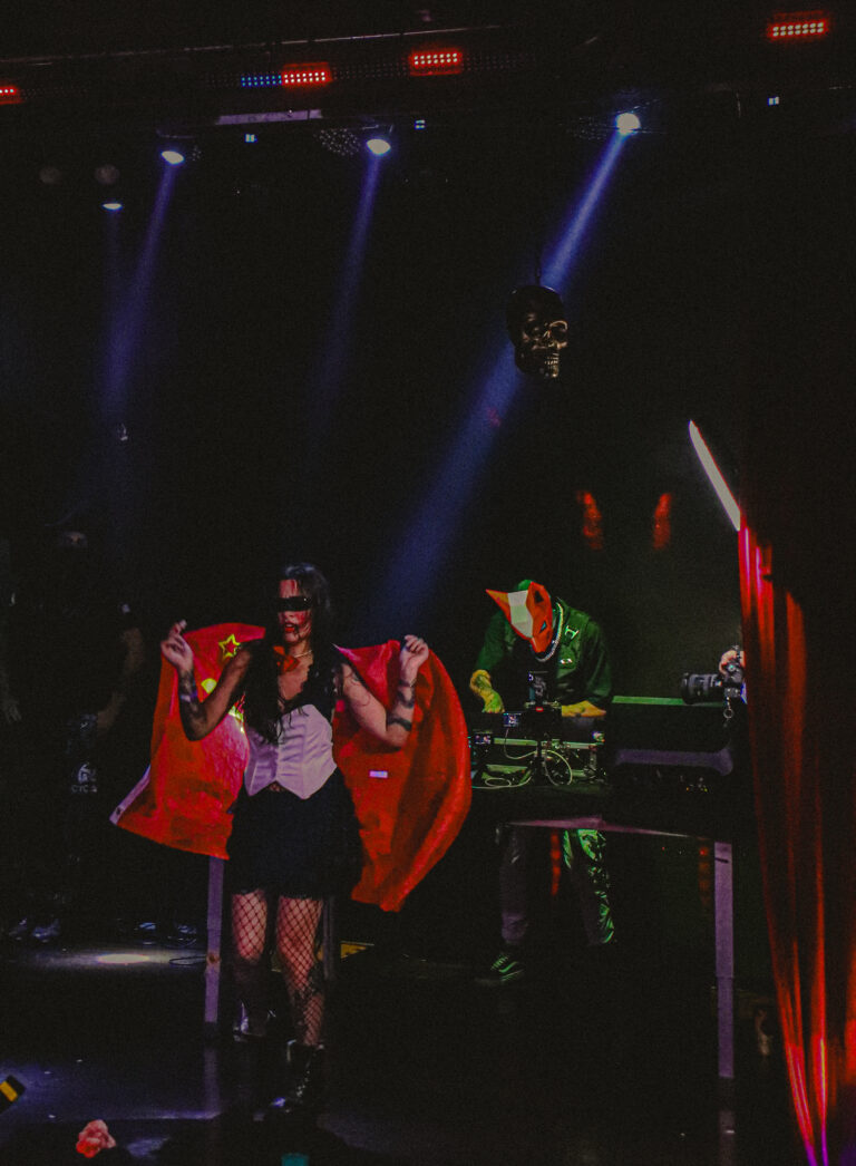 Artistas de capa vermelha dançam no palco escuro — Sad Baile Joker, Halloween em São Paulo, 17/10/2026