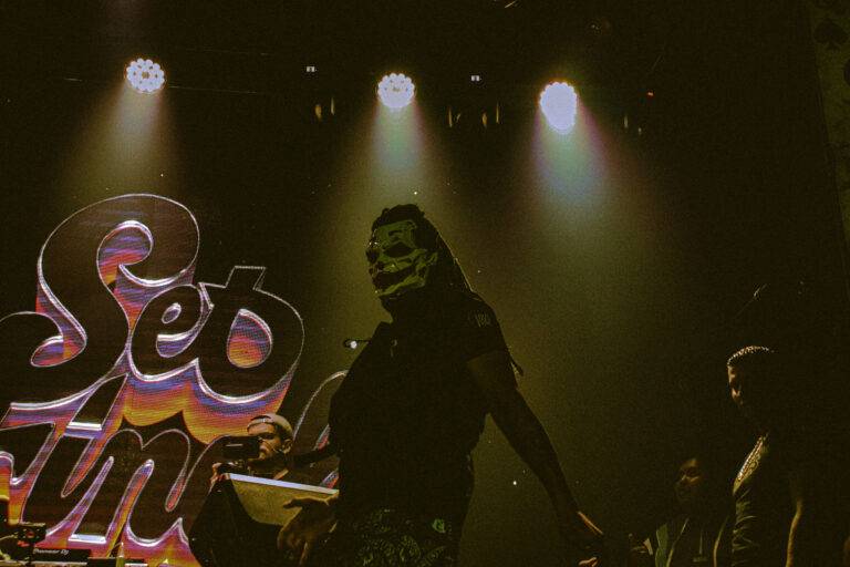 Artistas no palco diante do telão amarelo sob holofotes — Sad Baile Joker, Halloween em São Paulo, 17/10/2026