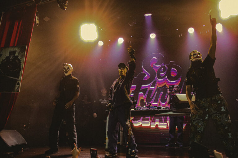 Palco com artistas mascarados sob luzes quentes — Sad Baile Joker, Halloween em São Paulo, 17/10/2026