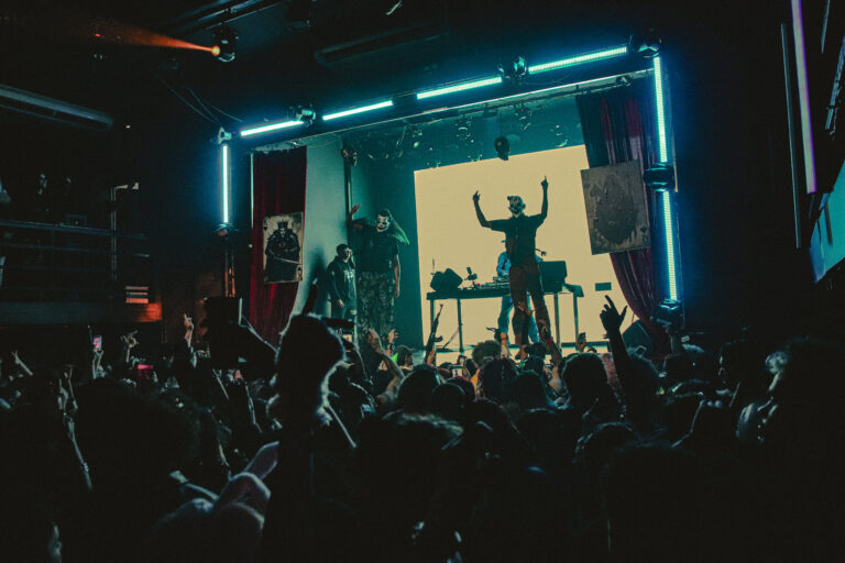 Palco emoldurado por néon azul e público em silhueta — Sad Baile Joker, Halloween em São Paulo, 17/10/2026