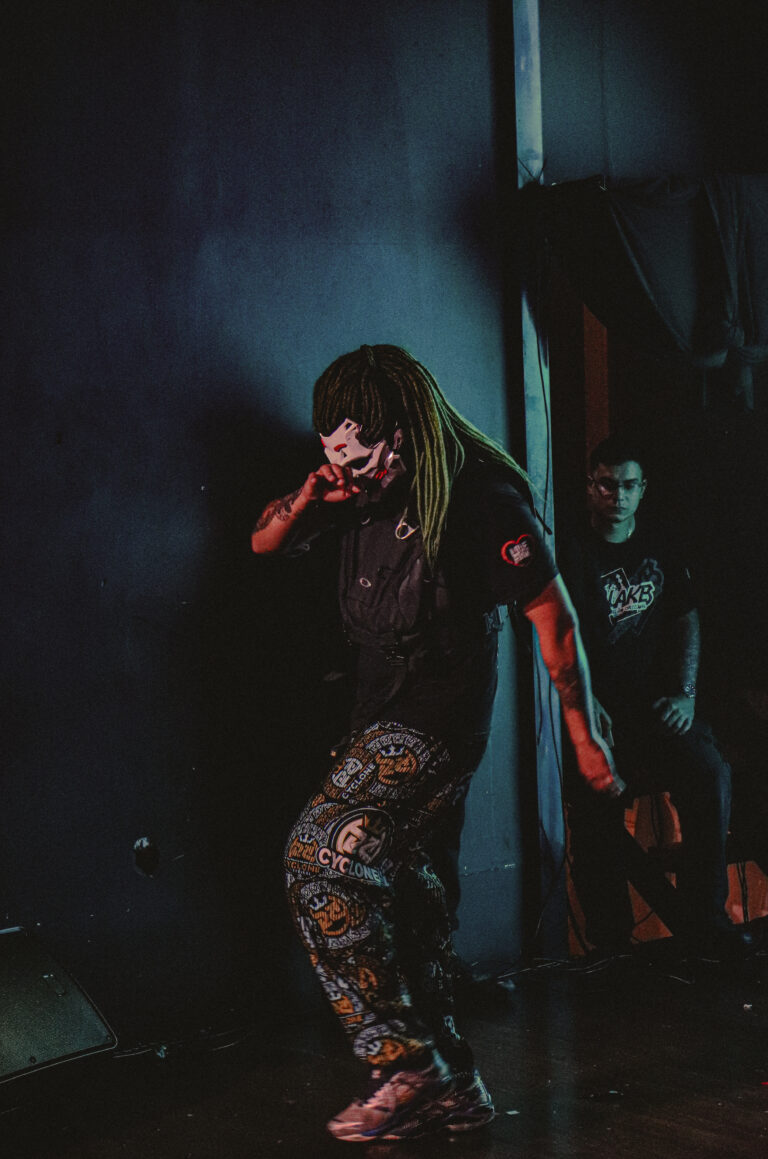 Artista de calça camuflada encostado na parede do palco — Sad Baile Joker, Halloween em São Paulo, 17/10/2026