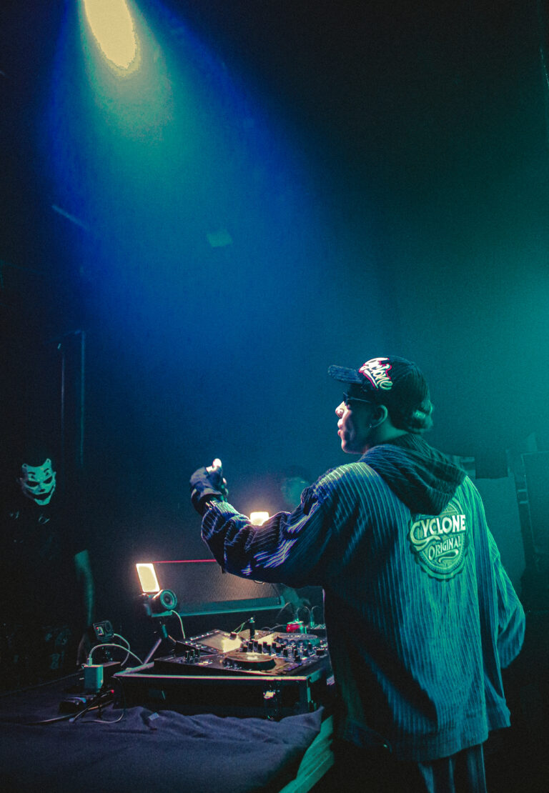 DJ de boné e moletom azul sob luz verde — Sad Baile Joker, Halloween em São Paulo, 17/10/2026