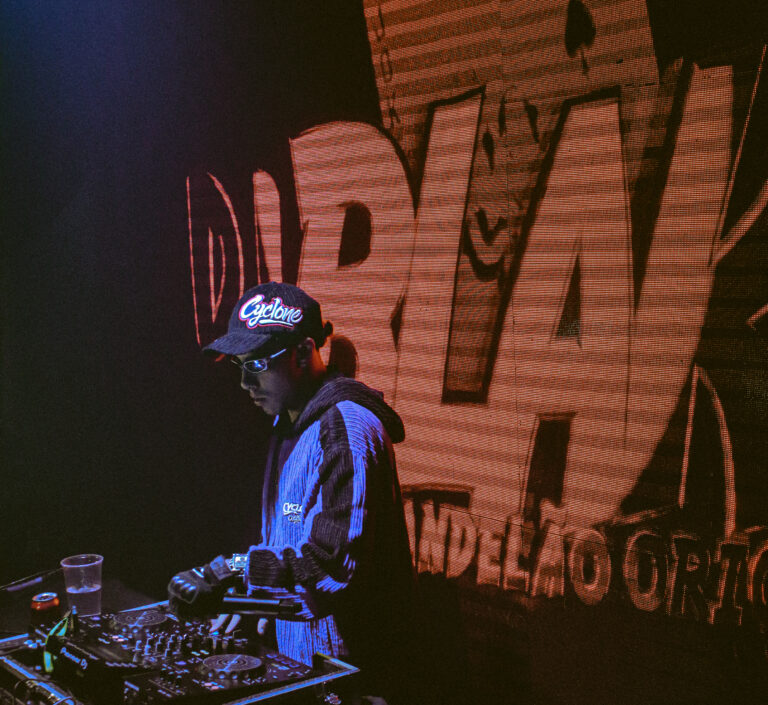 DJ de boné com telão laranja ao fundo — Sad Baile Joker, Halloween em São Paulo, 17/10/2026