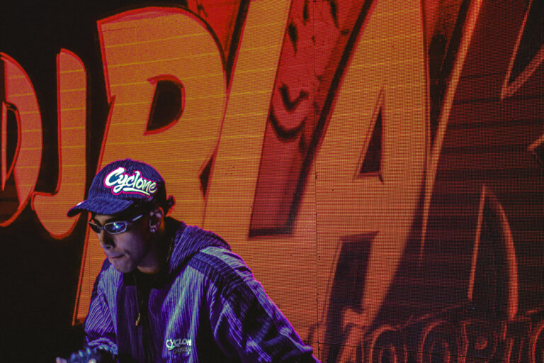 DJ de boné diante do telão laranja — Sad Baile Joker, Halloween em São Paulo, 17/10/2026