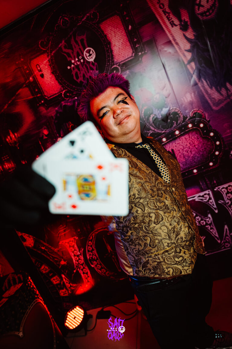 Rapaz de colete dourado lança cartas de baralho para a câmera — Sad Baile Joker, Halloween em São Paulo, 17/10/2026