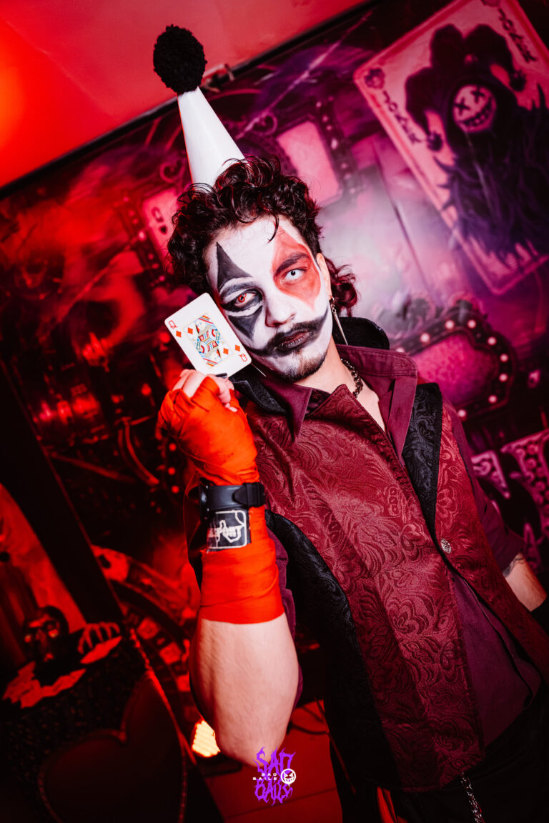 Palhaço segura carta de baralho sob luz vermelha — Sad Baile Joker, Halloween em São Paulo, 17/10/2026