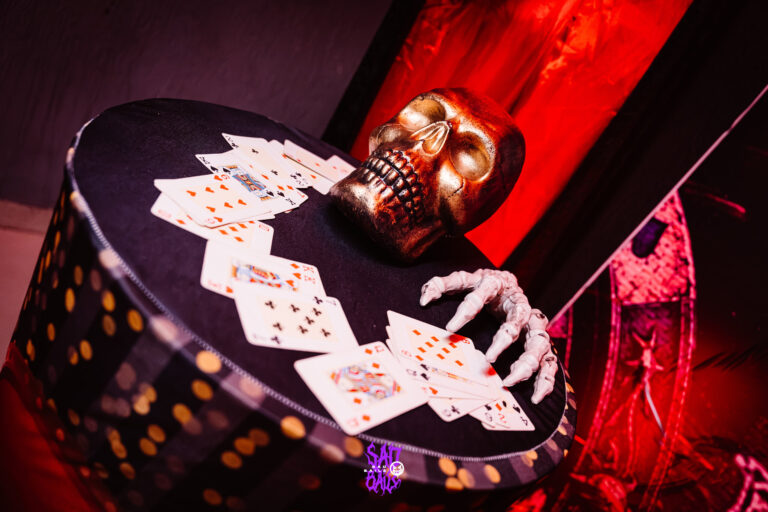Mão de esqueleto e cartas sobre a mesa decorada — Sad Baile Joker, Halloween em São Paulo, 17/10/2026