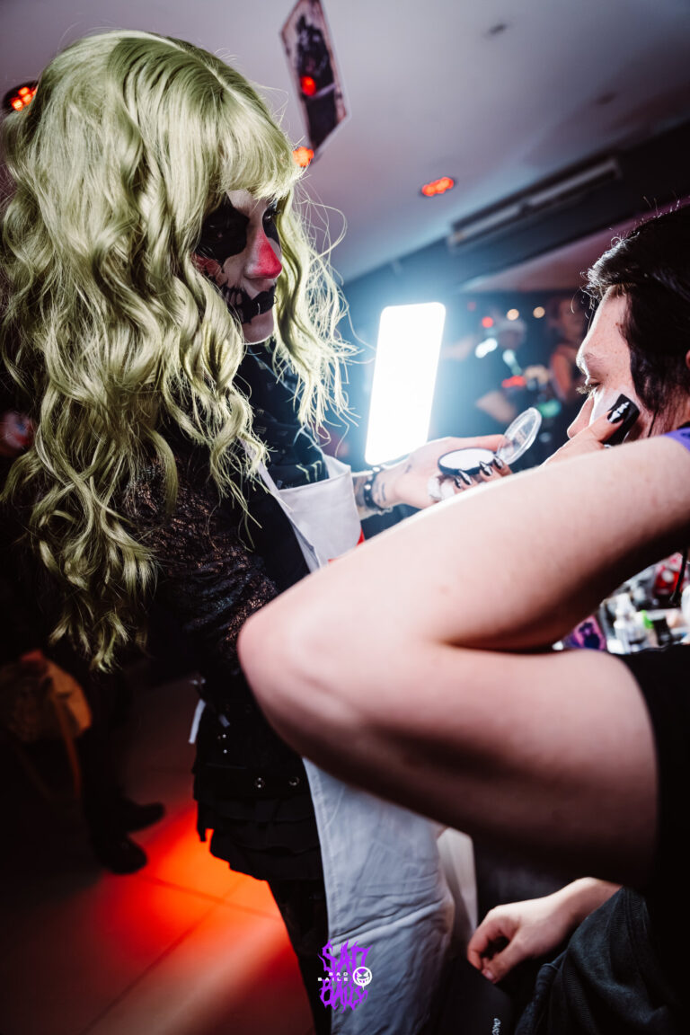 Maquiadora de peruca verde pinta o rosto de um participante — Sad Baile Joker, Halloween em São Paulo, 17/10/2026