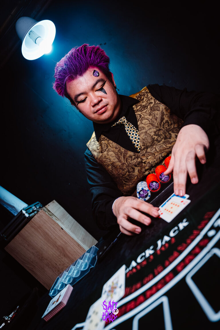 Crupiê de colete dourado na mesa de blackjack — Sad Baile Joker, Halloween em São Paulo, 17/10/2026
