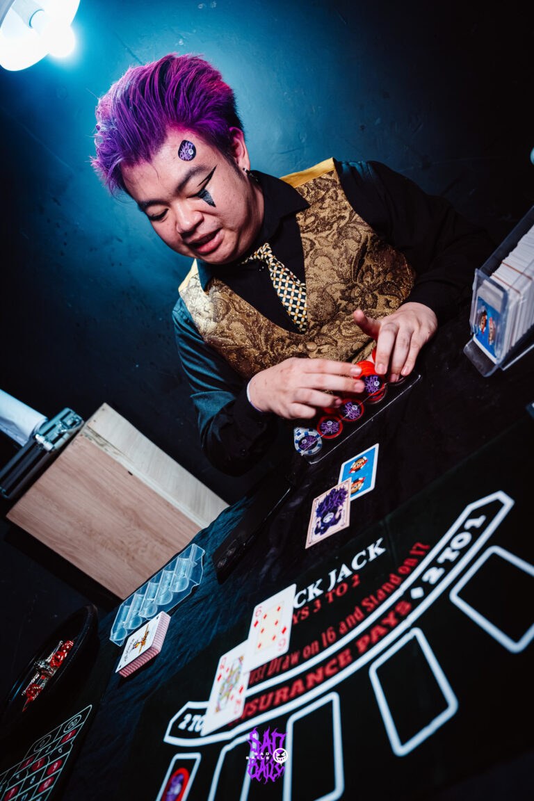 Crupiê de colete dourado e cabelo roxo sorri — Sad Baile Joker, Halloween em São Paulo, 17/10/2026