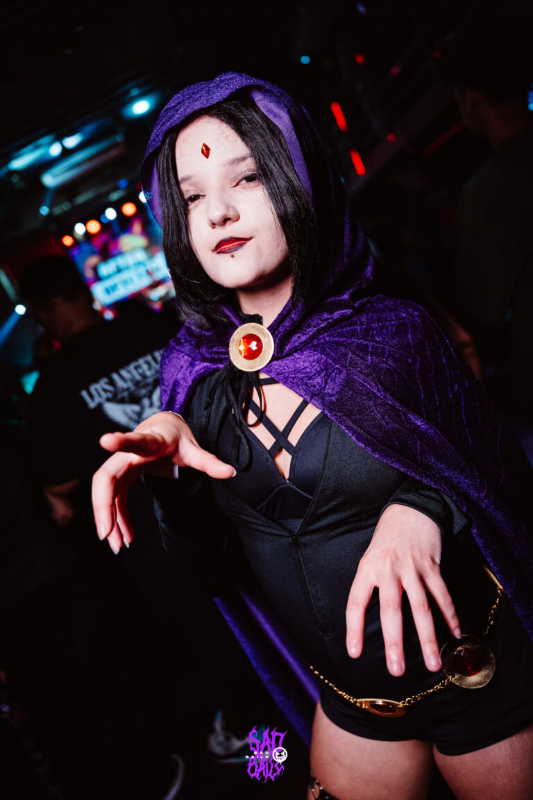 Ravena de capa roxa estende a mão para a câmera — Sad Baile Joker, Halloween em São Paulo, 17/10/2026