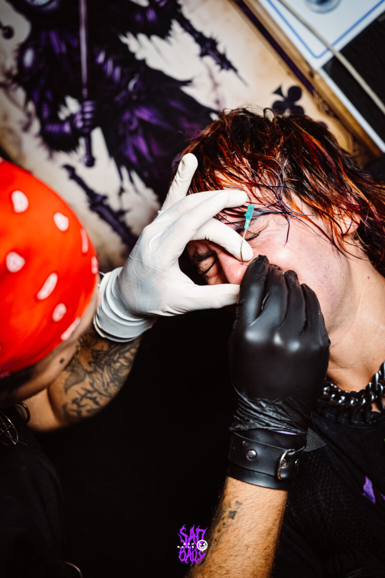 Piercer de luvas faz piercing em participante — Sad Baile Joker, Halloween em São Paulo, 17/10/2026