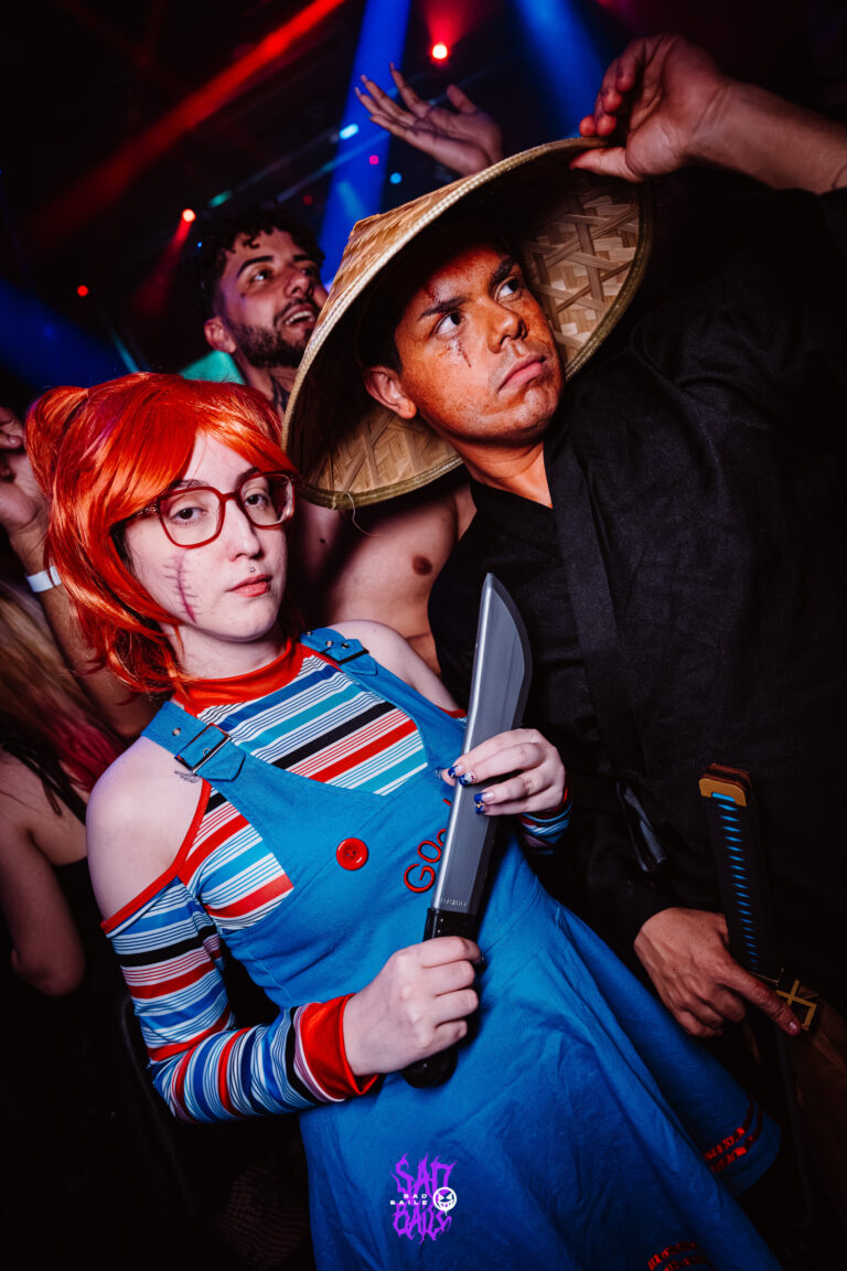 Fantasia de Chucky com faca ao lado de amigo de chapéu de palha — Sad Baile Joker, Halloween em São Paulo, 17/10/2026