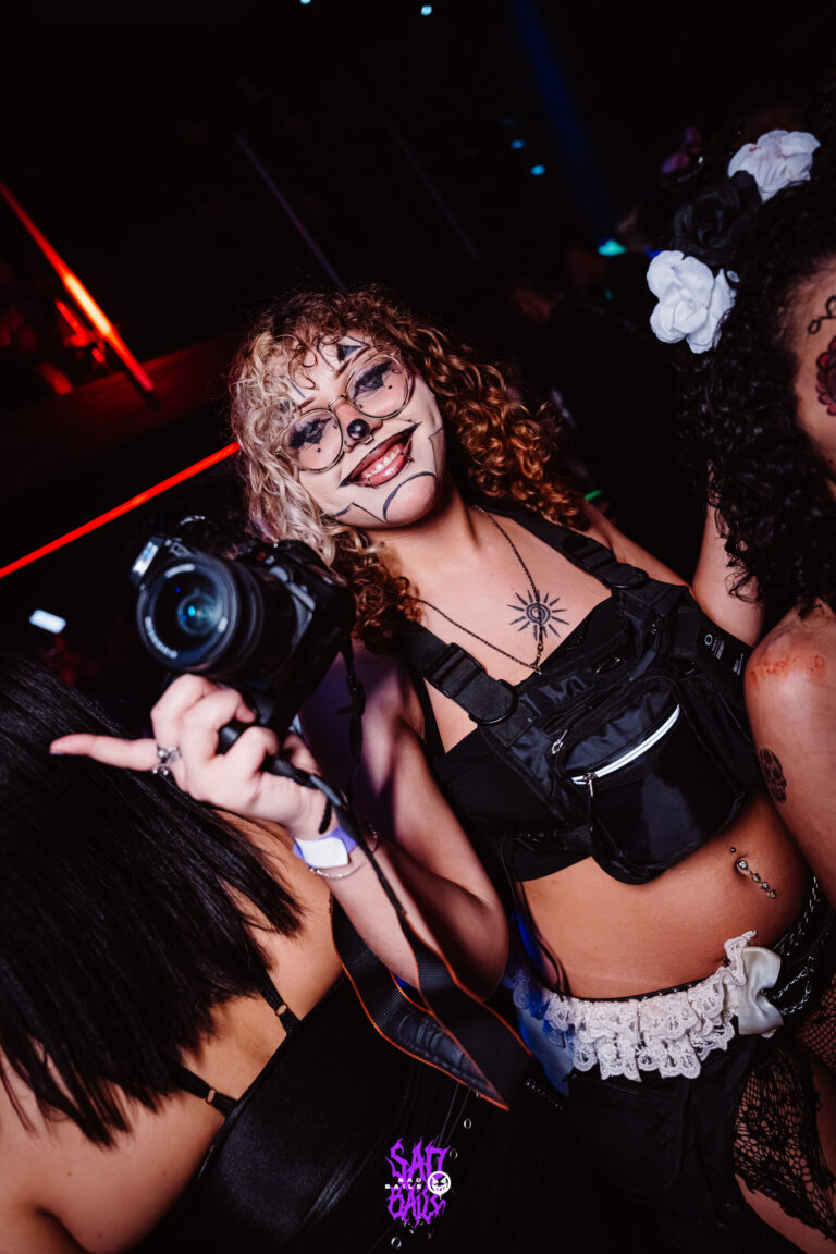 Garota de maquiagem de onça segura câmera fotográfica — Sad Baile Joker, Halloween em São Paulo, 17/10/2026