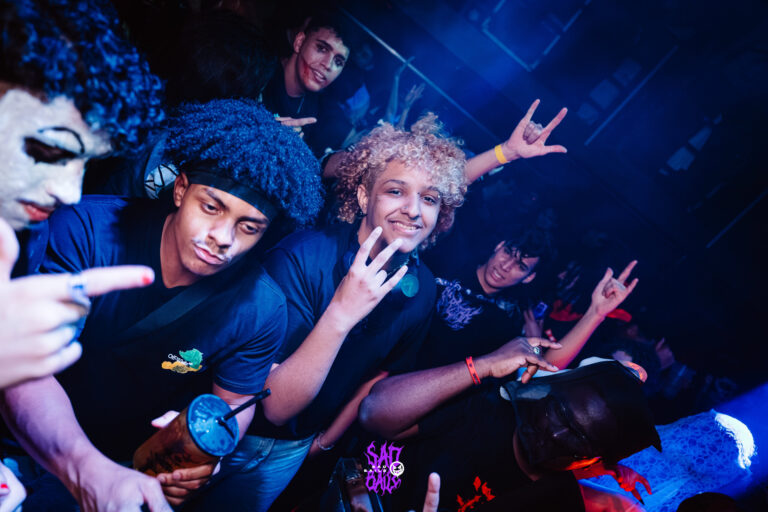 Amigos fazem pose na pista sob luz azul — Sad Baile Joker, Halloween em São Paulo, 17/10/2026