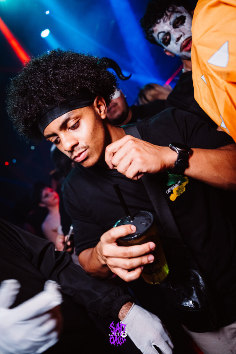 Rapaz de cabelo black power olha o celular — Sad Baile Joker, Halloween em São Paulo, 17/10/2026