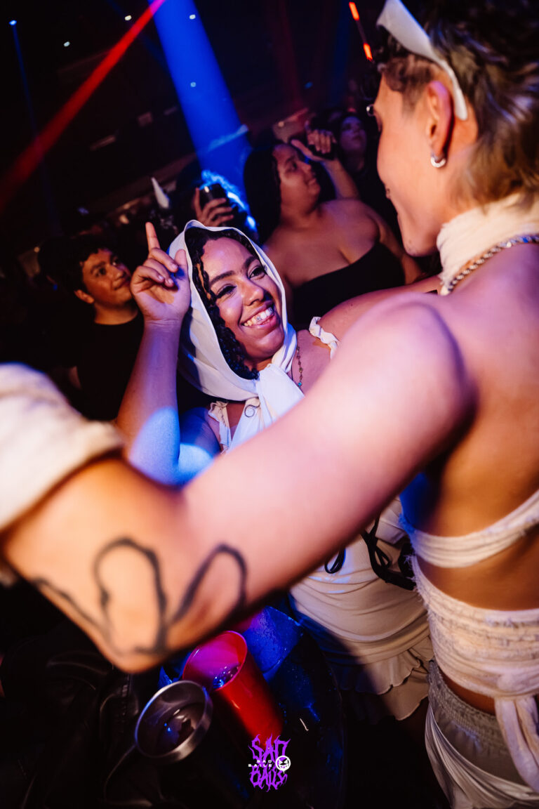 Amigas dançam abraçadas sob luz azul — Sad Baile Joker, Halloween em São Paulo, 17/10/2026