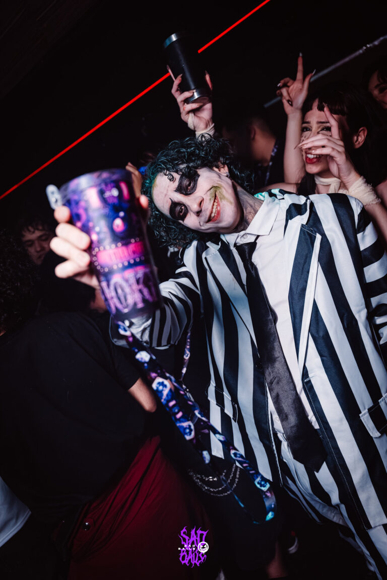 Rapaz de terno listrado ergue copo Joker — Sad Baile Joker, Halloween em São Paulo, 17/10/2026
