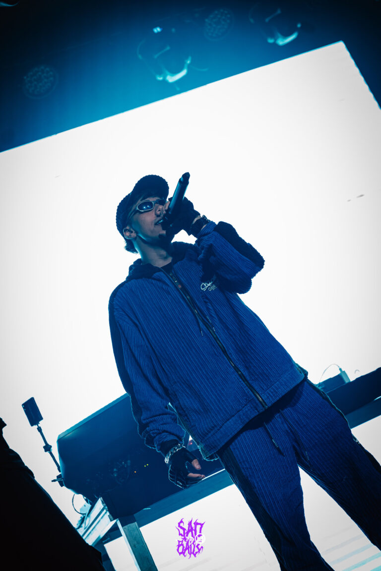 Rapper de boné e conjunto azul canta diante do telão branco — Sad Baile Joker, Halloween em São Paulo, 17/10/2026