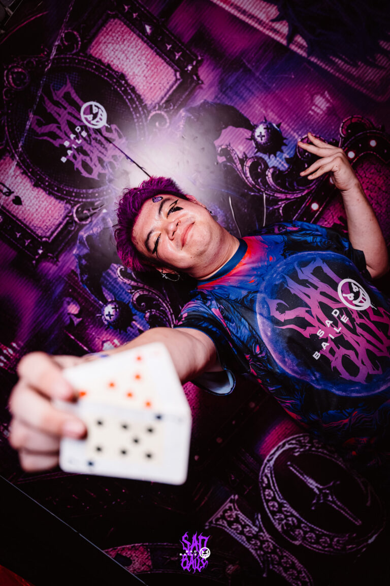 Rapaz de cabelo roxo segura carta de baralho no painel de Halloween — Sad Baile Joker, Halloween em São Paulo, 17/10/2026
