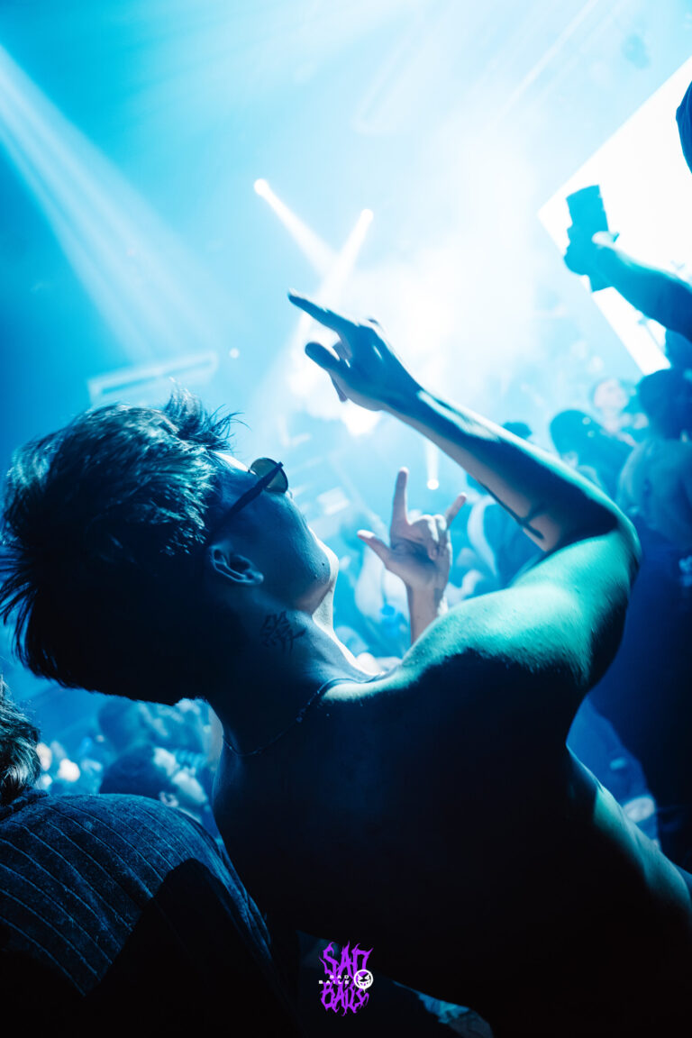 Rapaz ergue a mão diante do palco iluminado — Sad Baile Joker, Halloween em São Paulo, 17/10/2026