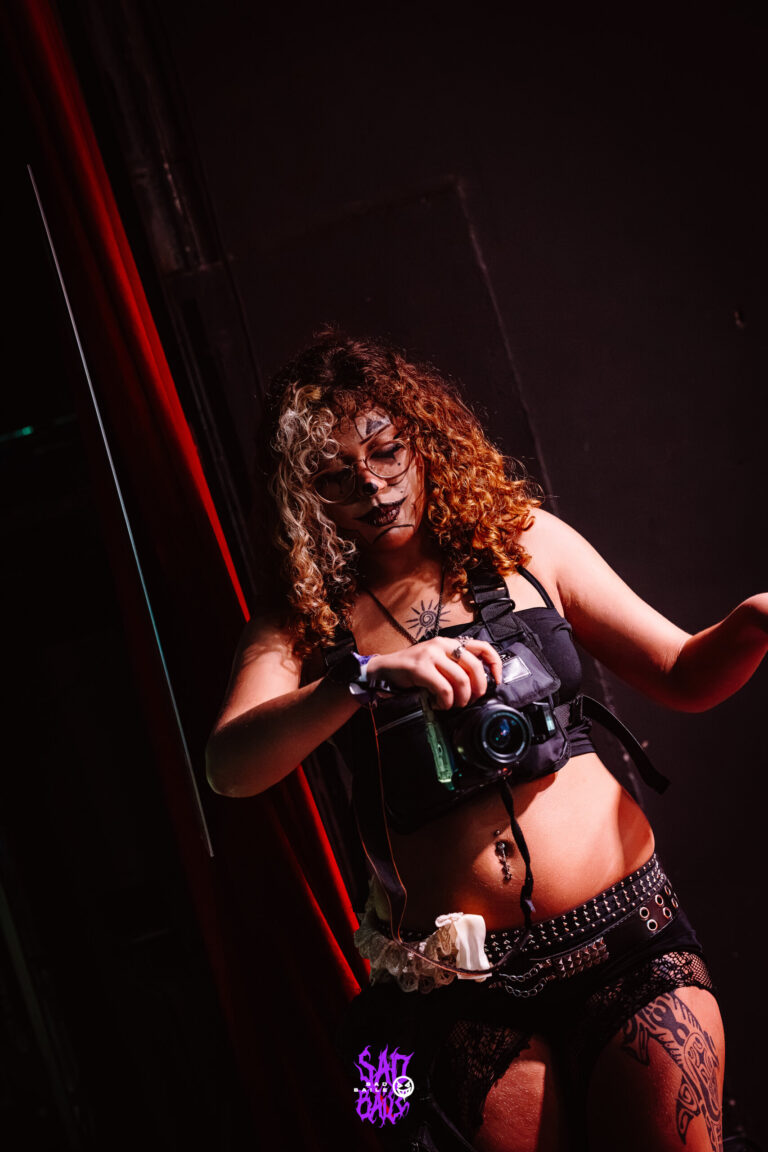 Garota de top preto com câmera fotográfica — Sad Baile Joker, Halloween em São Paulo, 17/10/2026